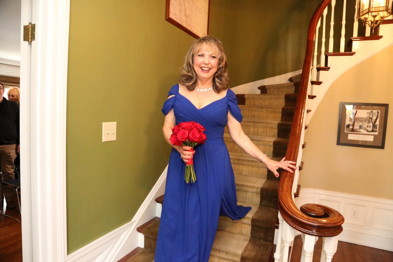 Alexanne smiles on the curved staircase in royal blue with her red rose bouquet