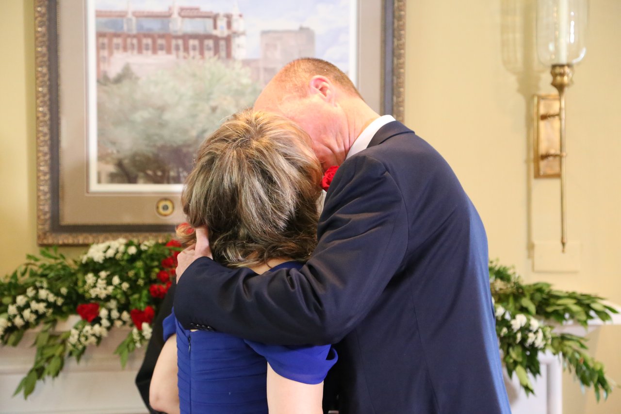 Alexanne and Tim embrace in front of the rose garland on the mantel