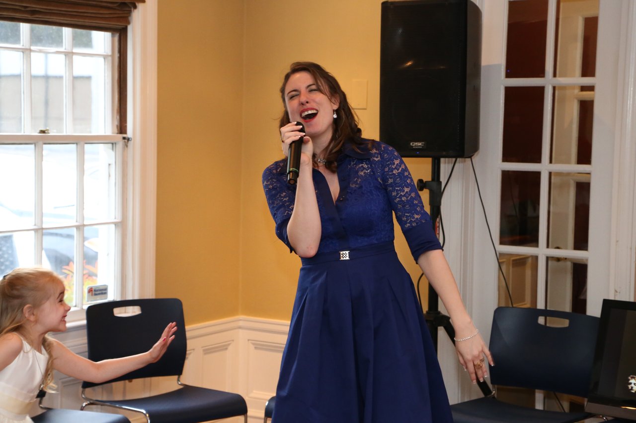 A guest in blue lace sings karaoke with her eyes closed