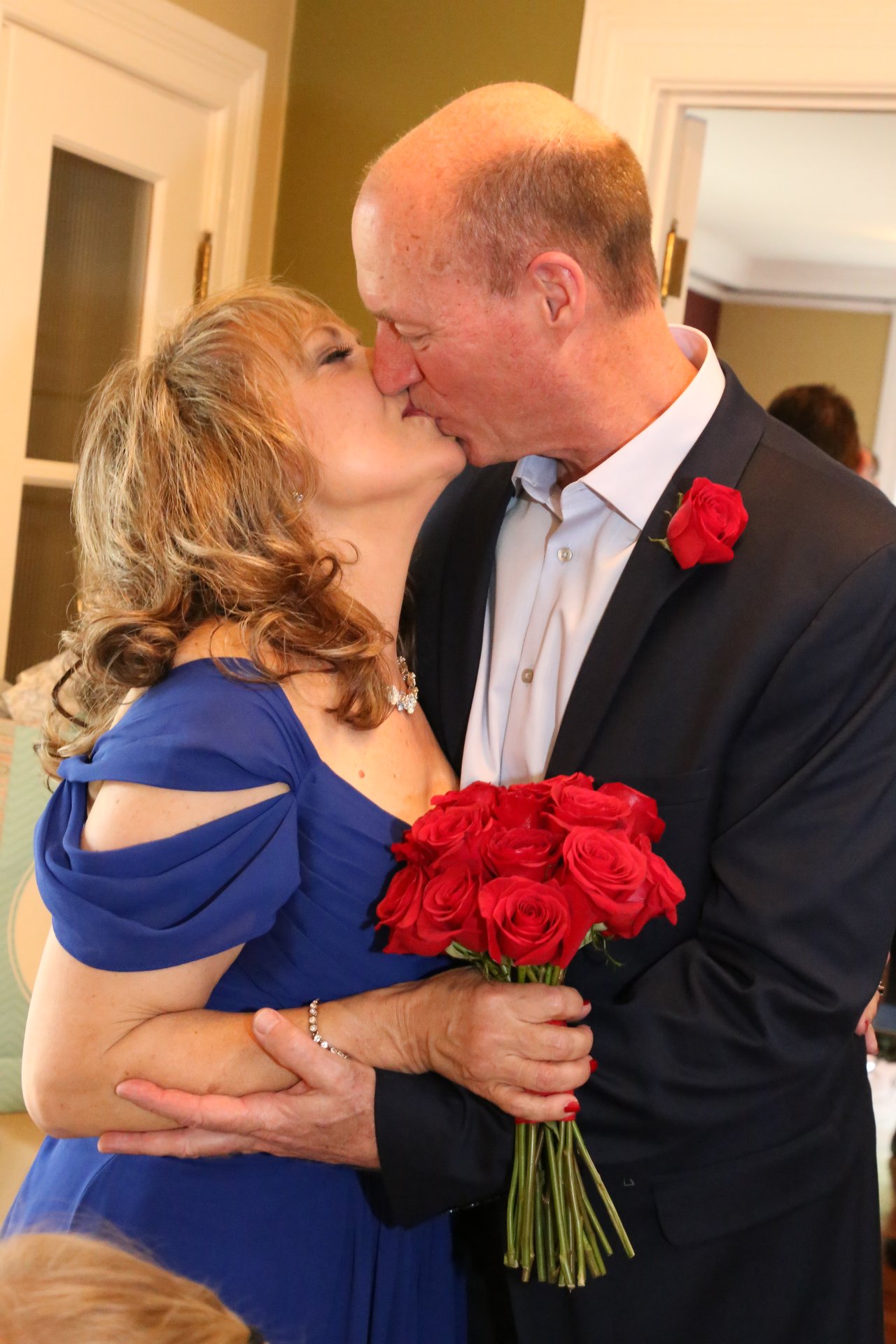 Alexanne and Tim kiss in the hallway with her red roses between them