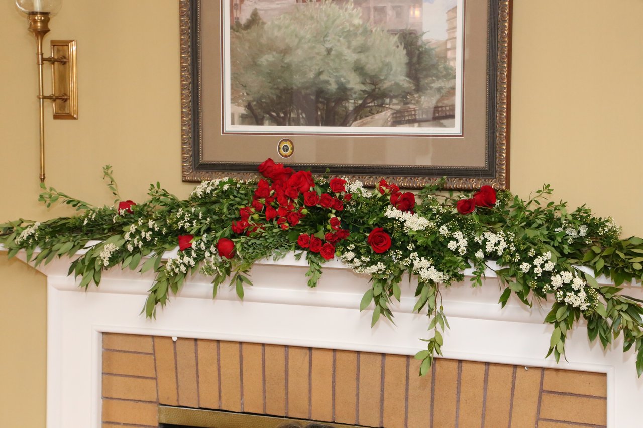 Red roses and white blossoms in a garland across the fireplace mantel
