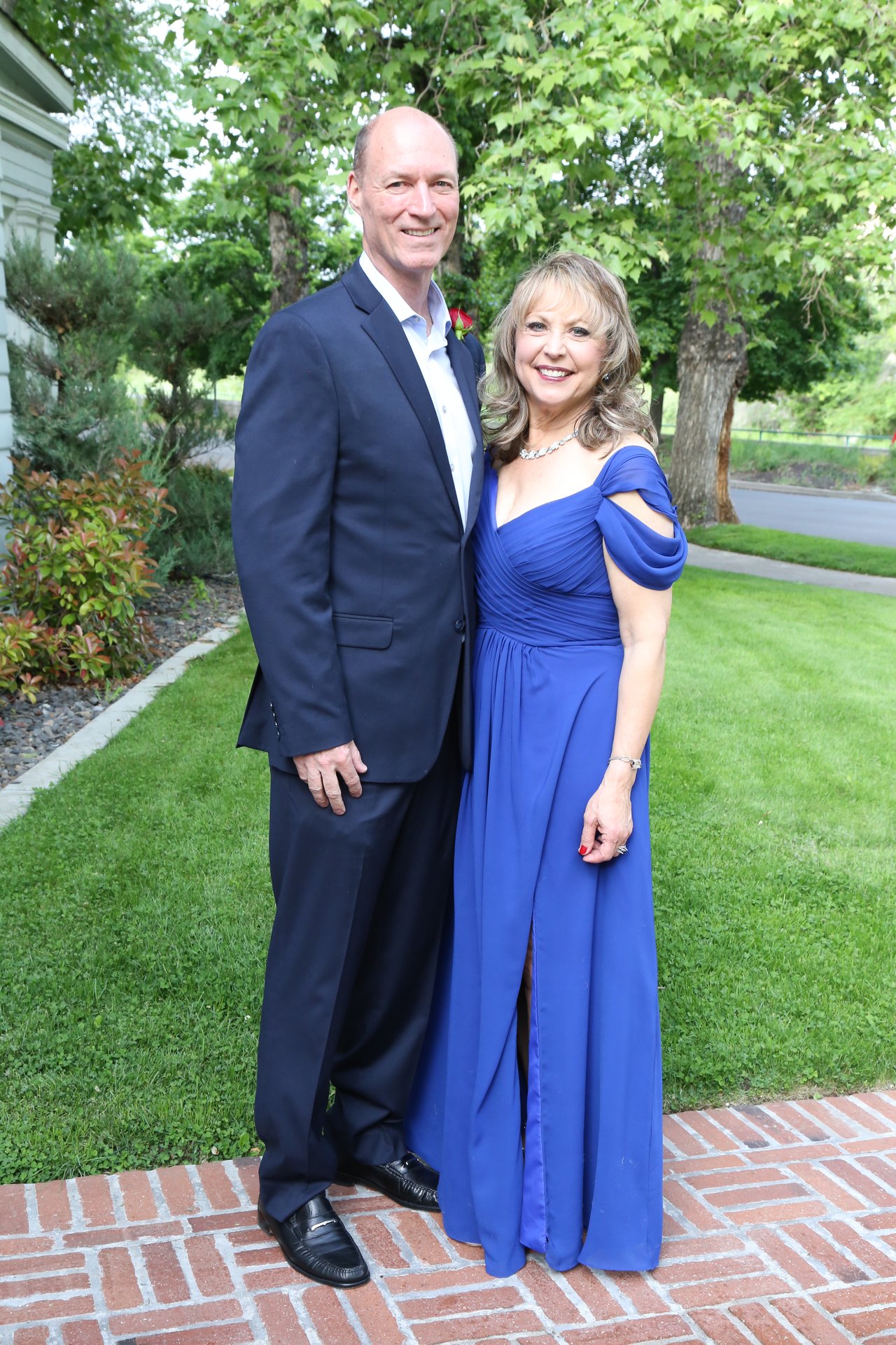 Tim and Alexanne stand on the brick path at the edge of the lawn