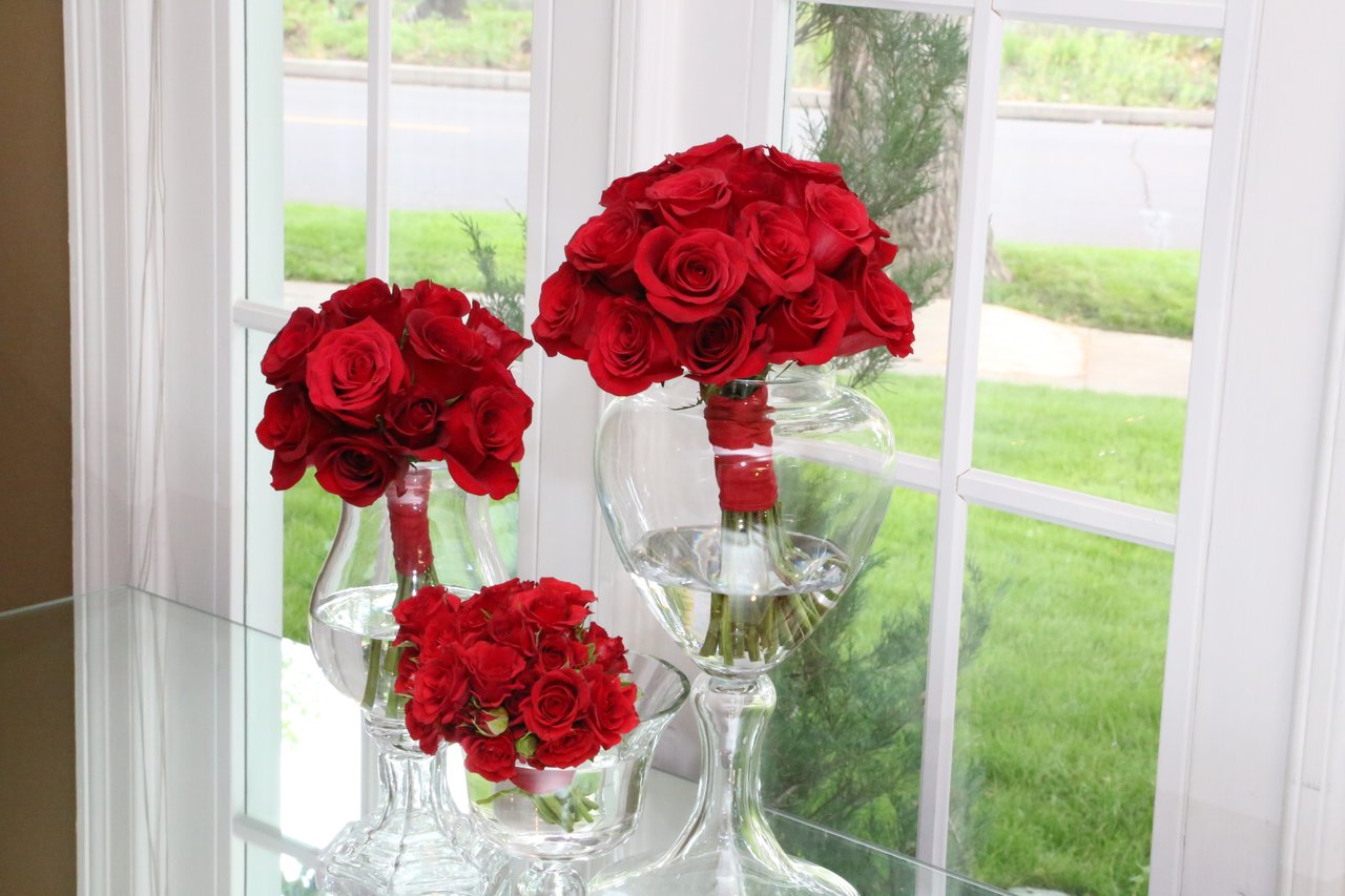 Red rose bouquets in glass vases beside a sunny window