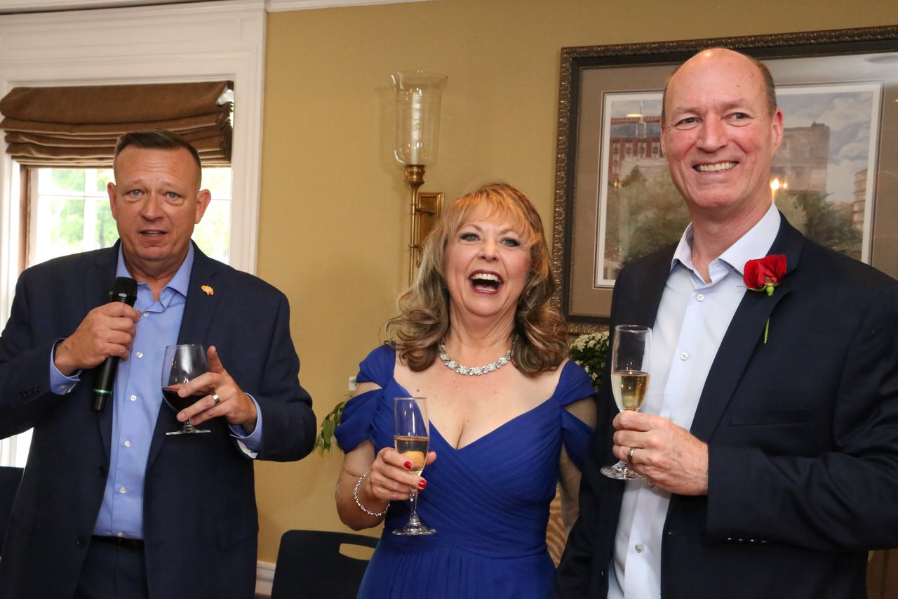 A friend gives a toast while Alexanne and Tim laugh beside him