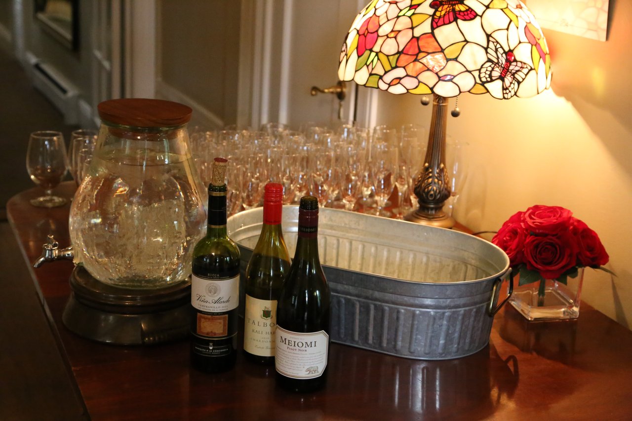 Wine, glasses and a red rose set out under a stained glass lamp