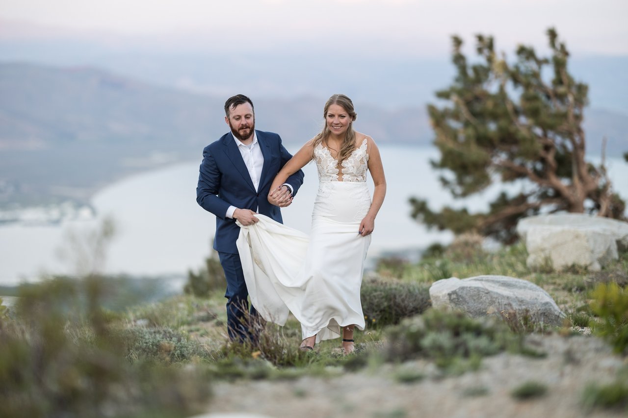 Ali holds her dress as they walk the ridge, both laughing