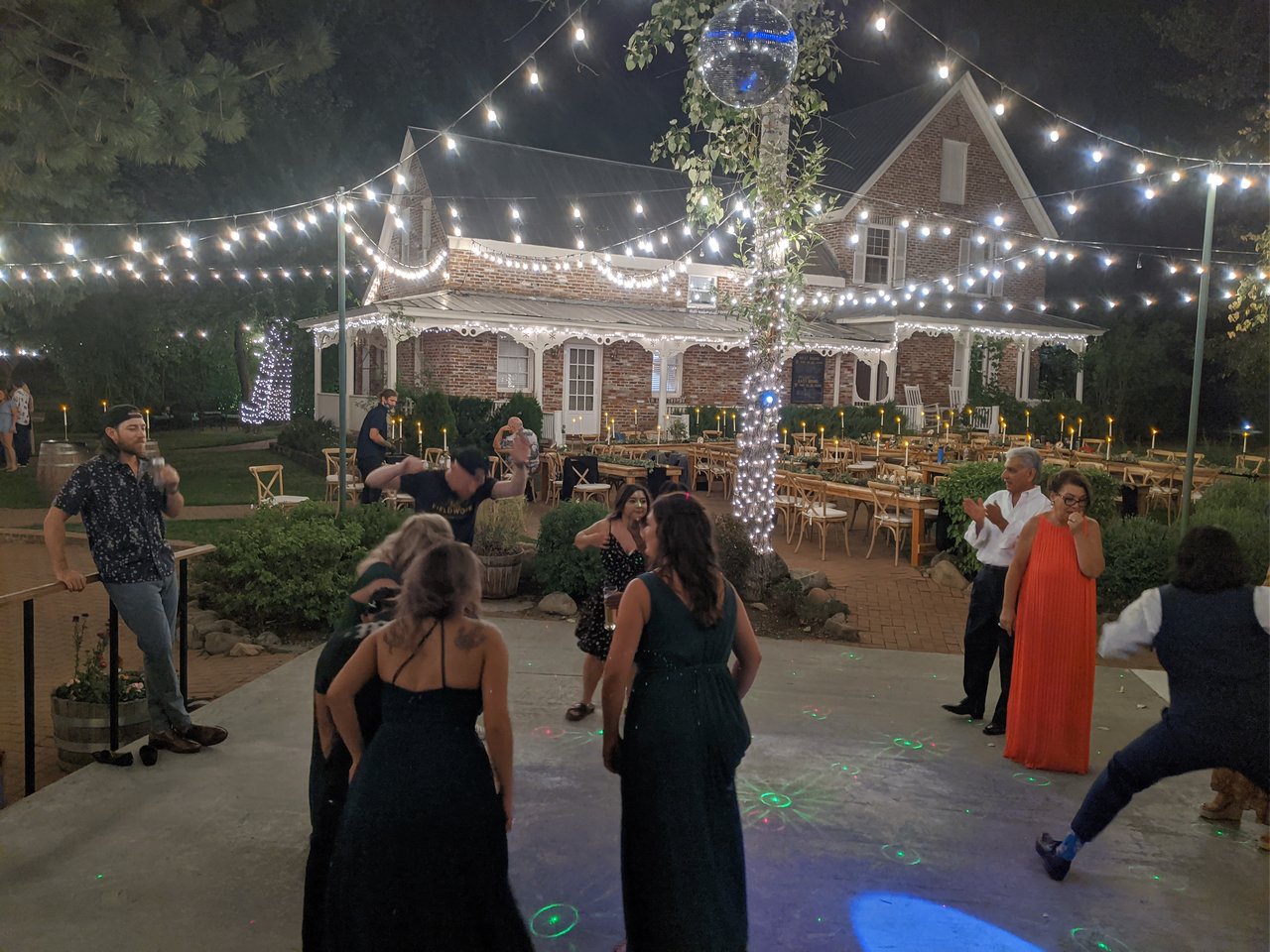 Guests dance under the mirror ball and string lights in front of the lit brick house at night