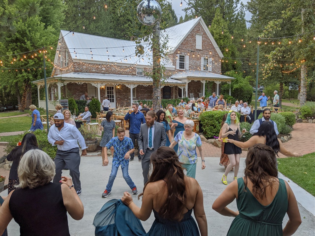 Guests of every age dance on the patio in front of the brick house
