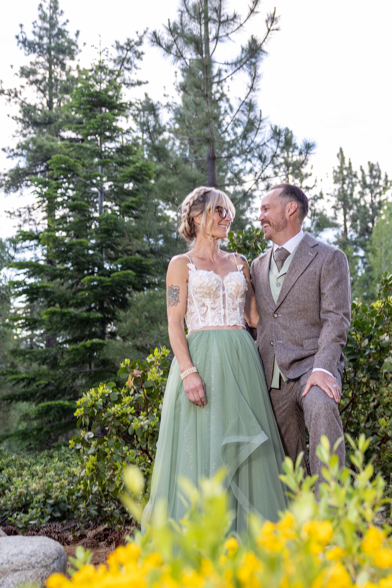 Amy and Justin smiling beside yellow wildflowers in the forest