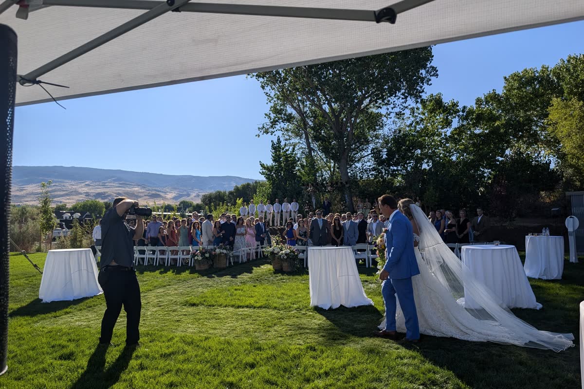 Wyatt walks Anabella down the grass aisle past seated guests, with the Sierra foothills behind them