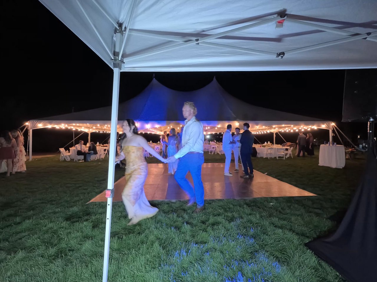 Two guests dance hand in hand on the lawn dance floor under blue lights