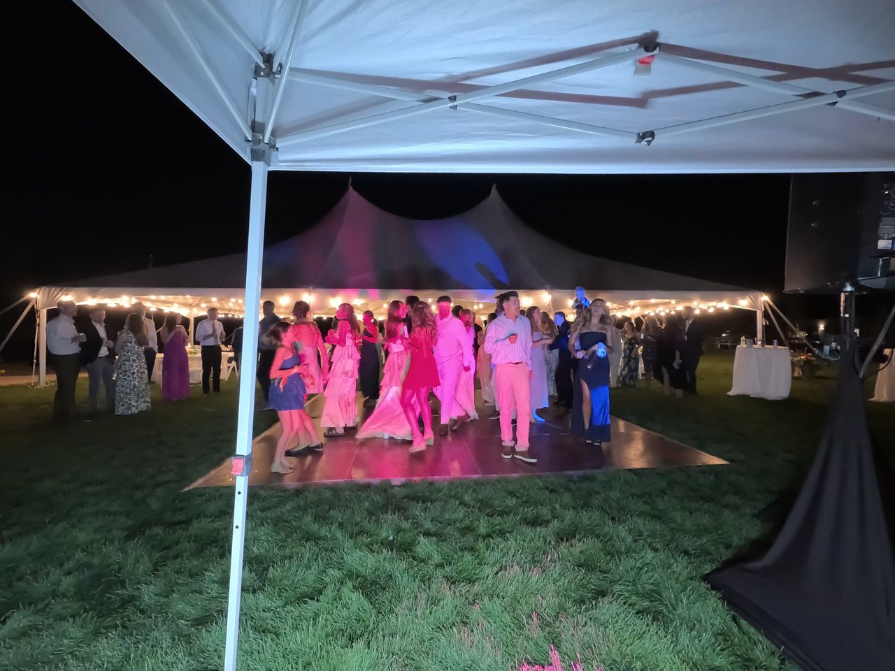 A full dance floor glows pink and purple beside the string lit tent
