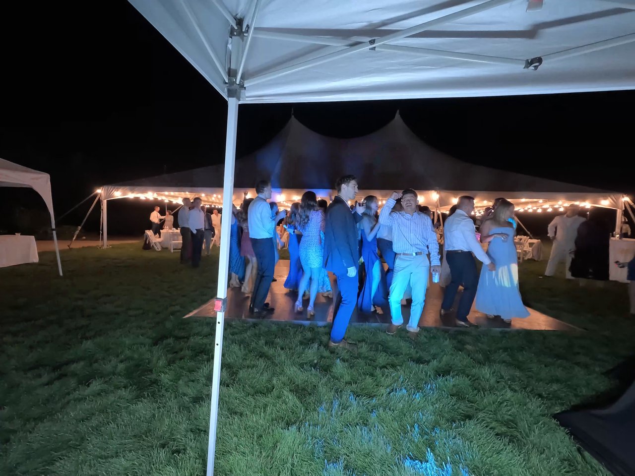 Guests dance under blue lights on the lawn dance floor in front of the tent