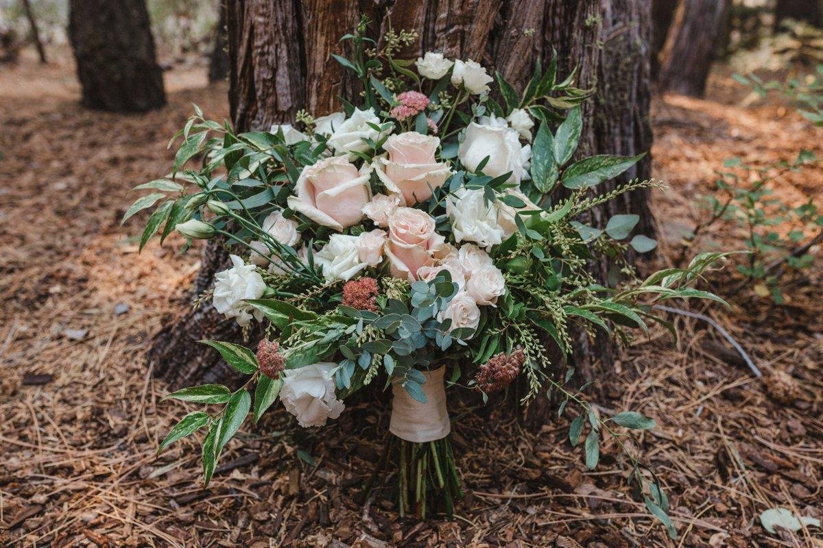 Angela's bouquet of blush and white roses rests against a pine trunk, photo by Composing Reality Photography