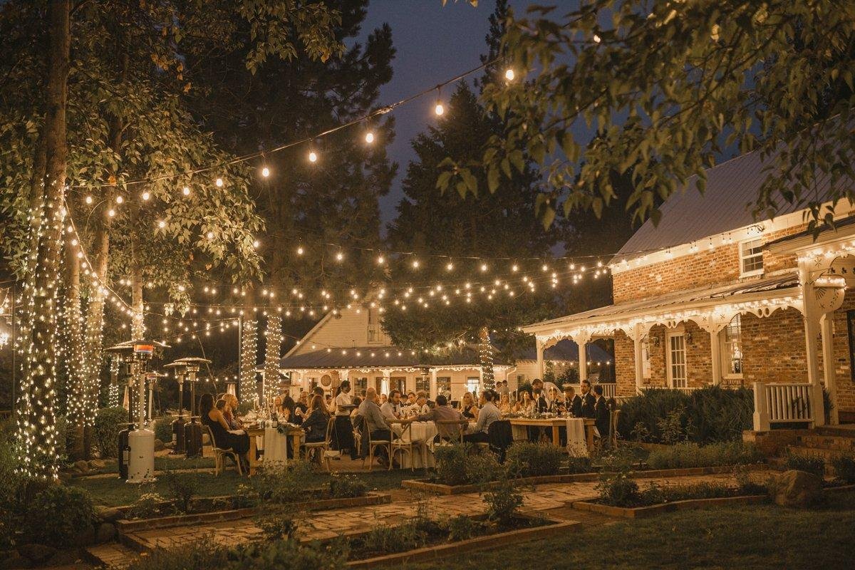 Guests at dinner on the patio under glowing string lights at night, photo by Composing Reality Photography
