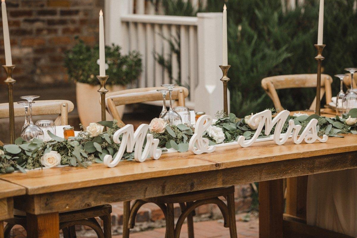 A Mr and Mrs sign among roses and eucalyptus on the sweetheart table with brass candlesticks, photo by Composing Reality Photography