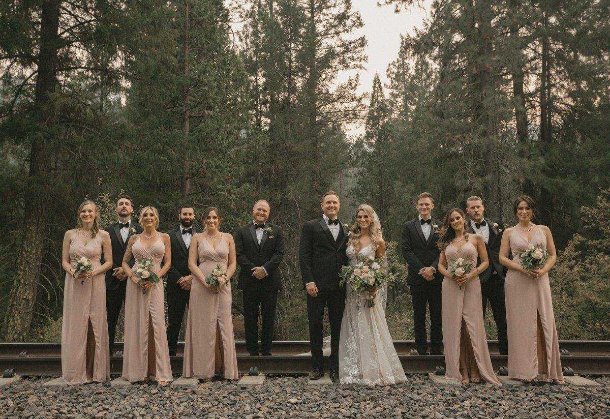 Angela, Stephen and their wedding party lined up on the railroad tracks among the pines, photo by Composing Reality Photography