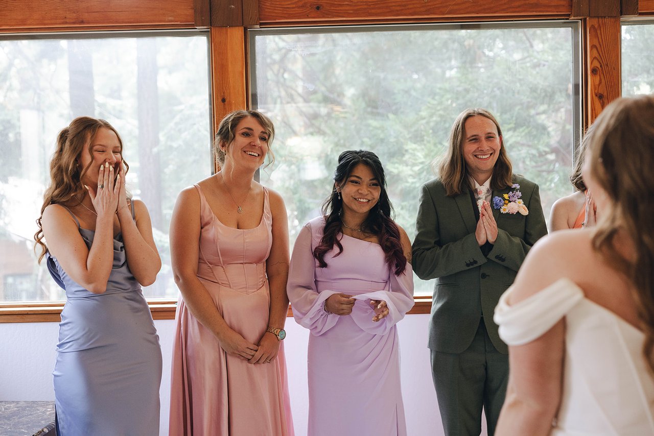 Bridesmaids cover their mouths and smile as they see Autumn in her dress