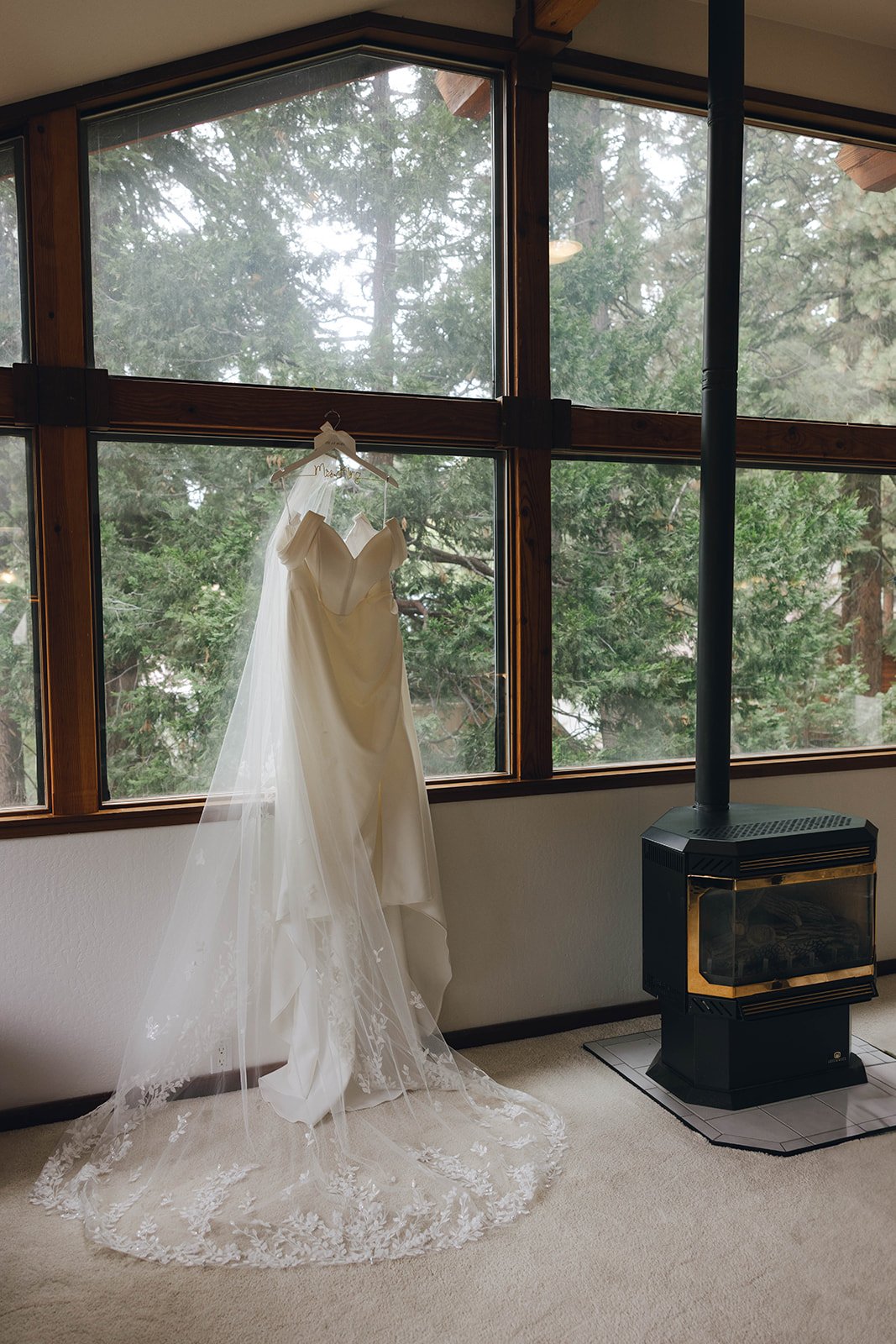 Autumn's wedding dress and veil hang in a tall window beside a wood stove