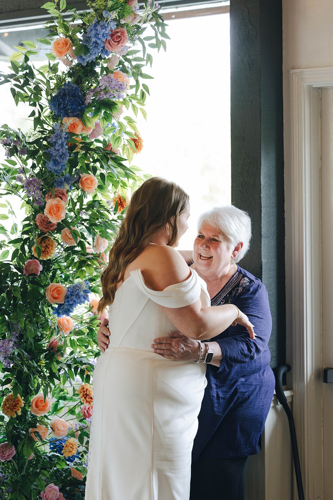 Autumn hugs a smiling guest beside a tall arrangement of flowers