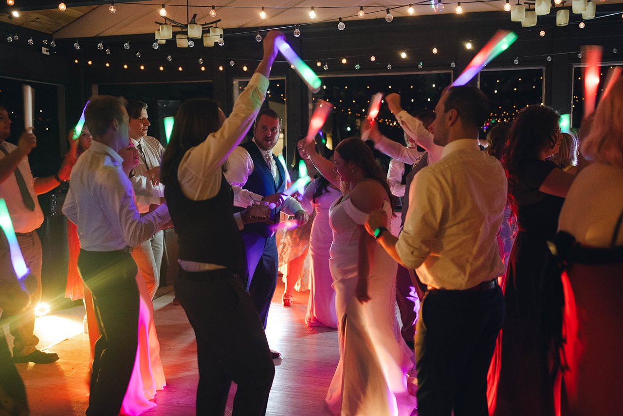 Guests wave colored glow sticks on the dance floor under the string lights