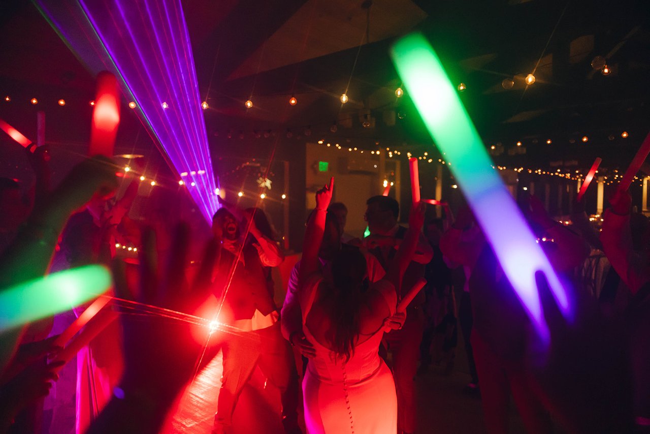 A fan of purple laser beams over a red lit dance floor full of glow sticks