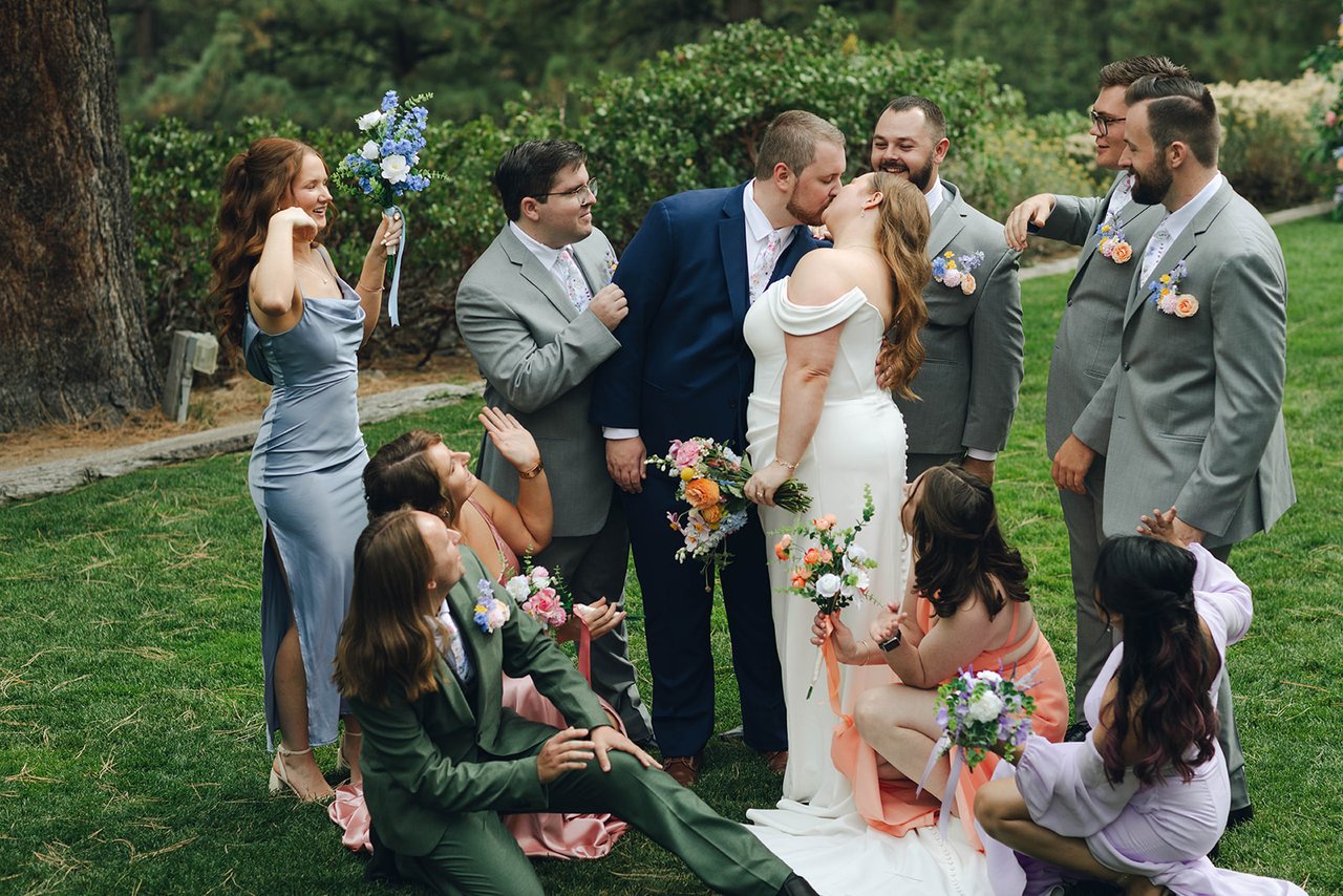 Autumn and Peter kiss while their wedding party crowds around them on the lawn