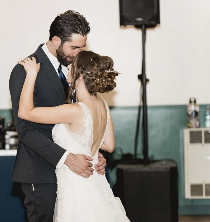 John and Caitlyn share a kiss as they slow dance, her braided updo and lace gown in the hall light