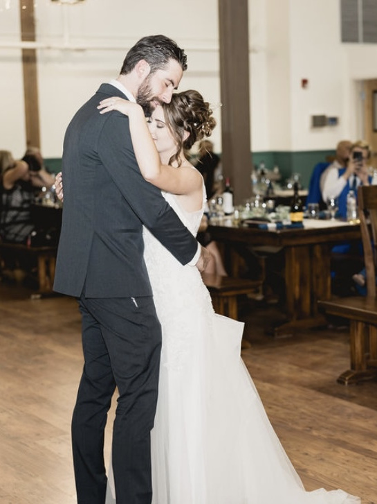John holds Caitlyn close in a slow dance, her eyes closed, on the wood floor at Camp WeChMe