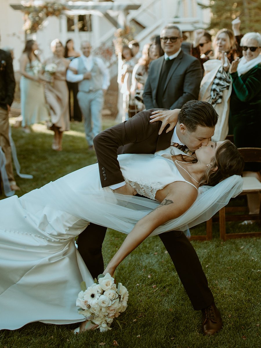 Devin dips Emily for a kiss in the aisle as their guests cheer behind them