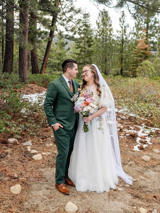 Madison and Adam stand together in the pines with patches of snow behind them, photo by GOT Photography