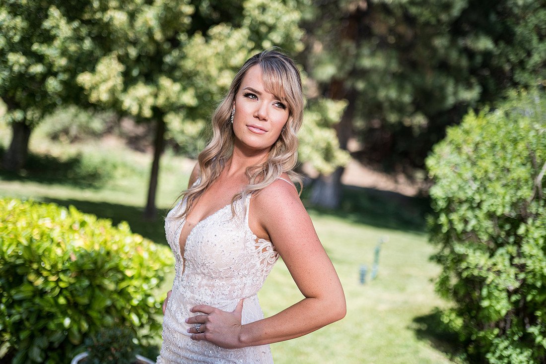 Correen poses on the lawn in her gown with a hand on her hip, pines behind her