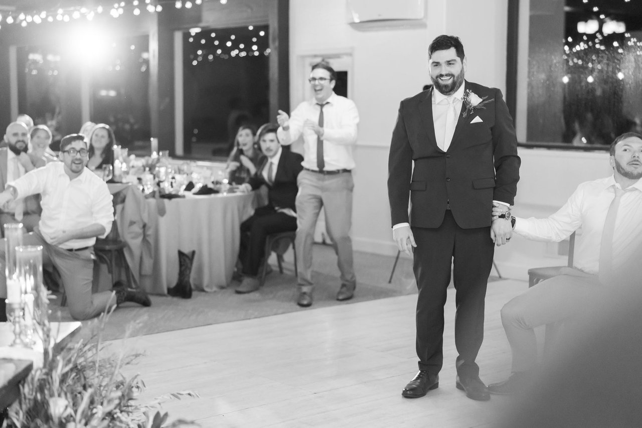 A black and white photo of Brandon grinning as guests cheer behind him