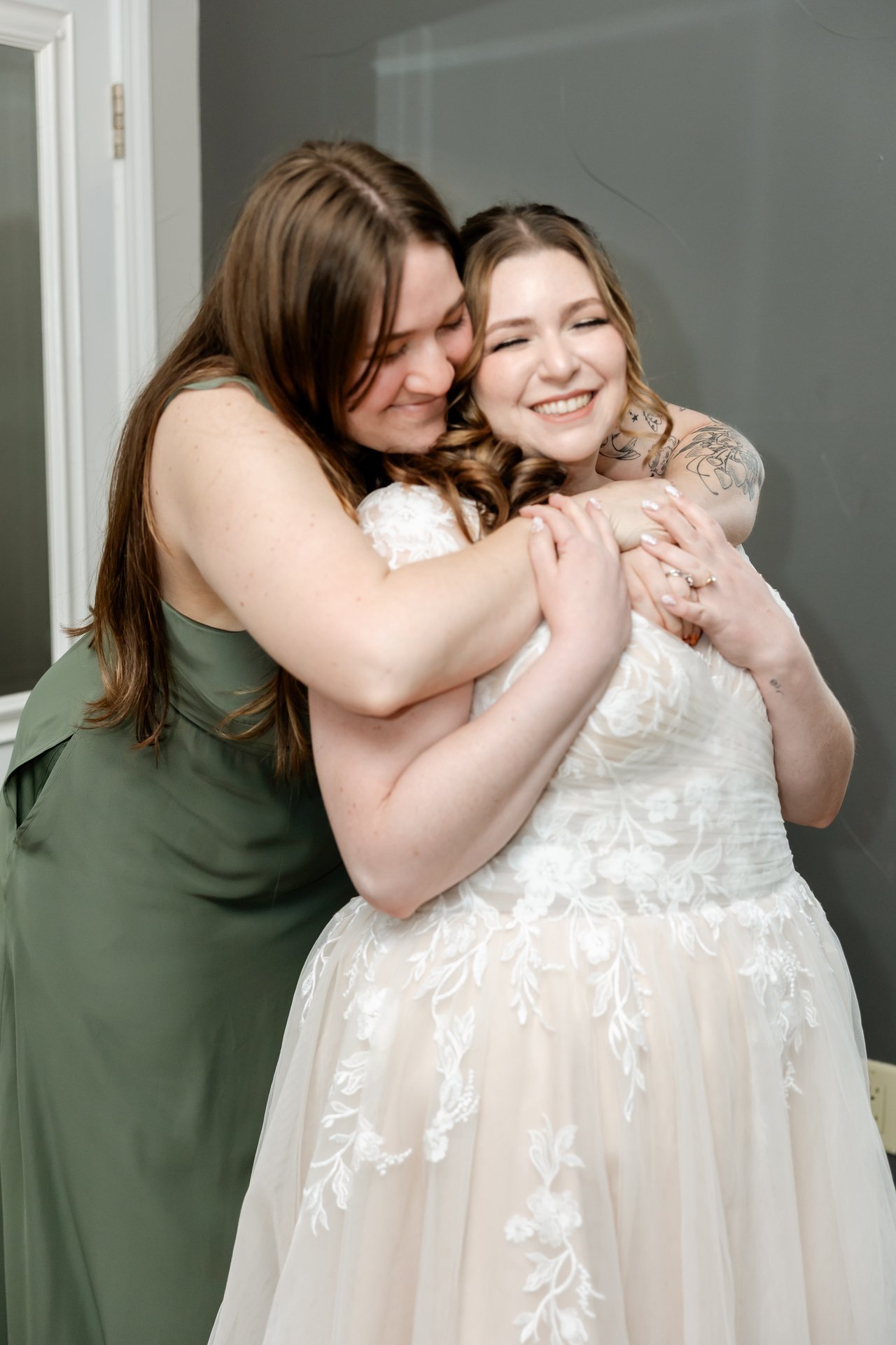 A bridesmaid in green hugs Danielle from behind as they both smile