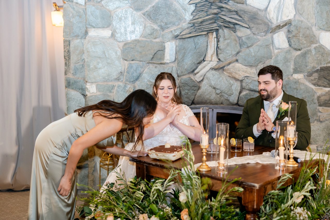 A bridesmaid bows at the sweetheart table as Danielle laughs