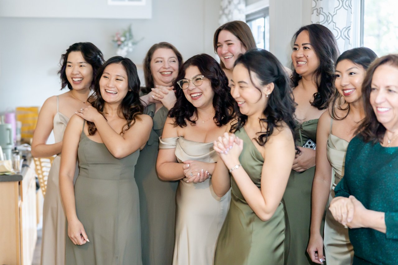 Danielle's bridesmaids in sage dresses smile as they see her for the first time