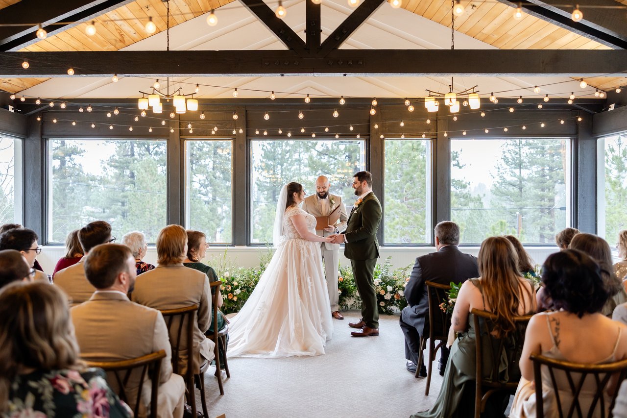The ceremony in front of the tall windows and string lights at the Tannenbaum Event Center