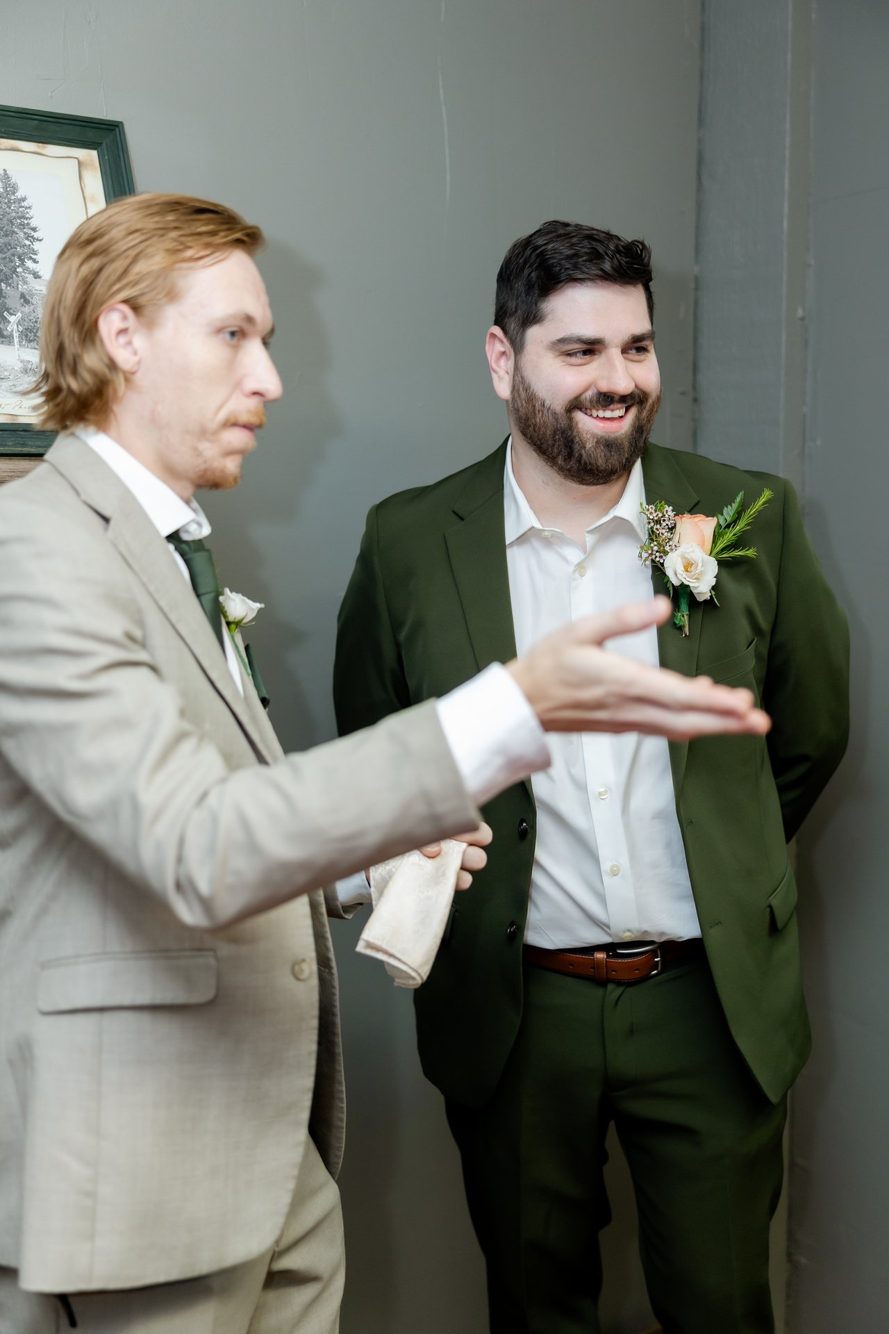 A groomsman in a tan suit cracks a joke while Brandon laughs in his green suit