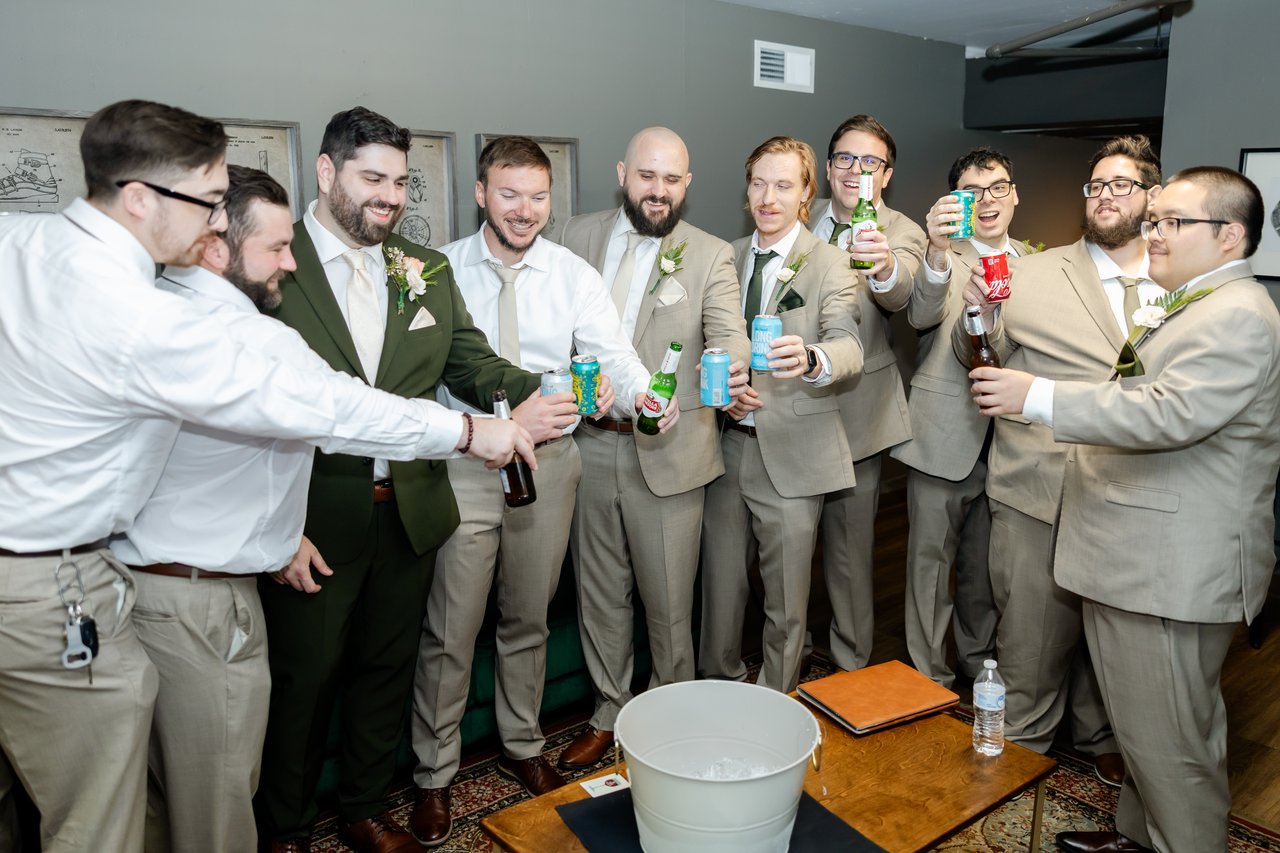 Brandon and his groomsmen raise their cans together in a cheers