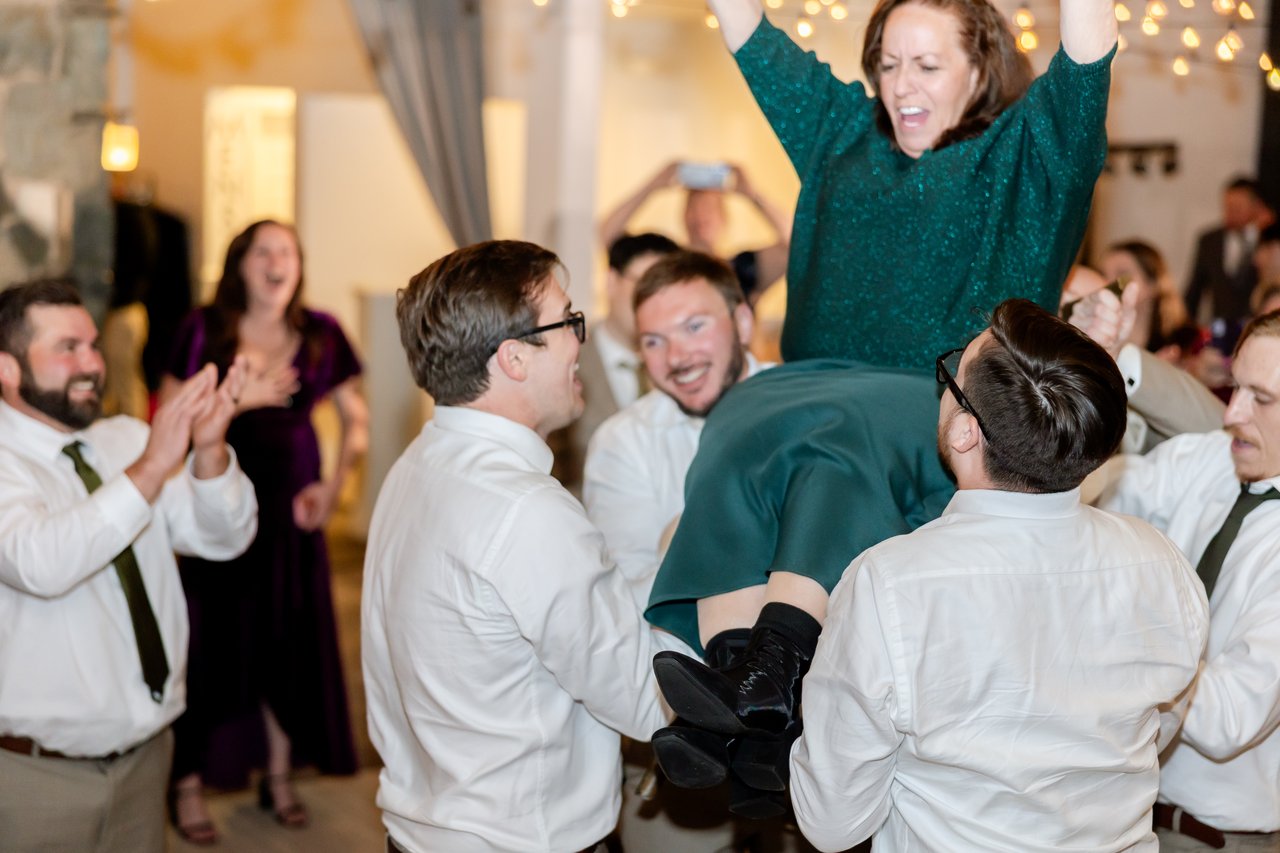 A guest in green is lifted in a chair while everyone claps