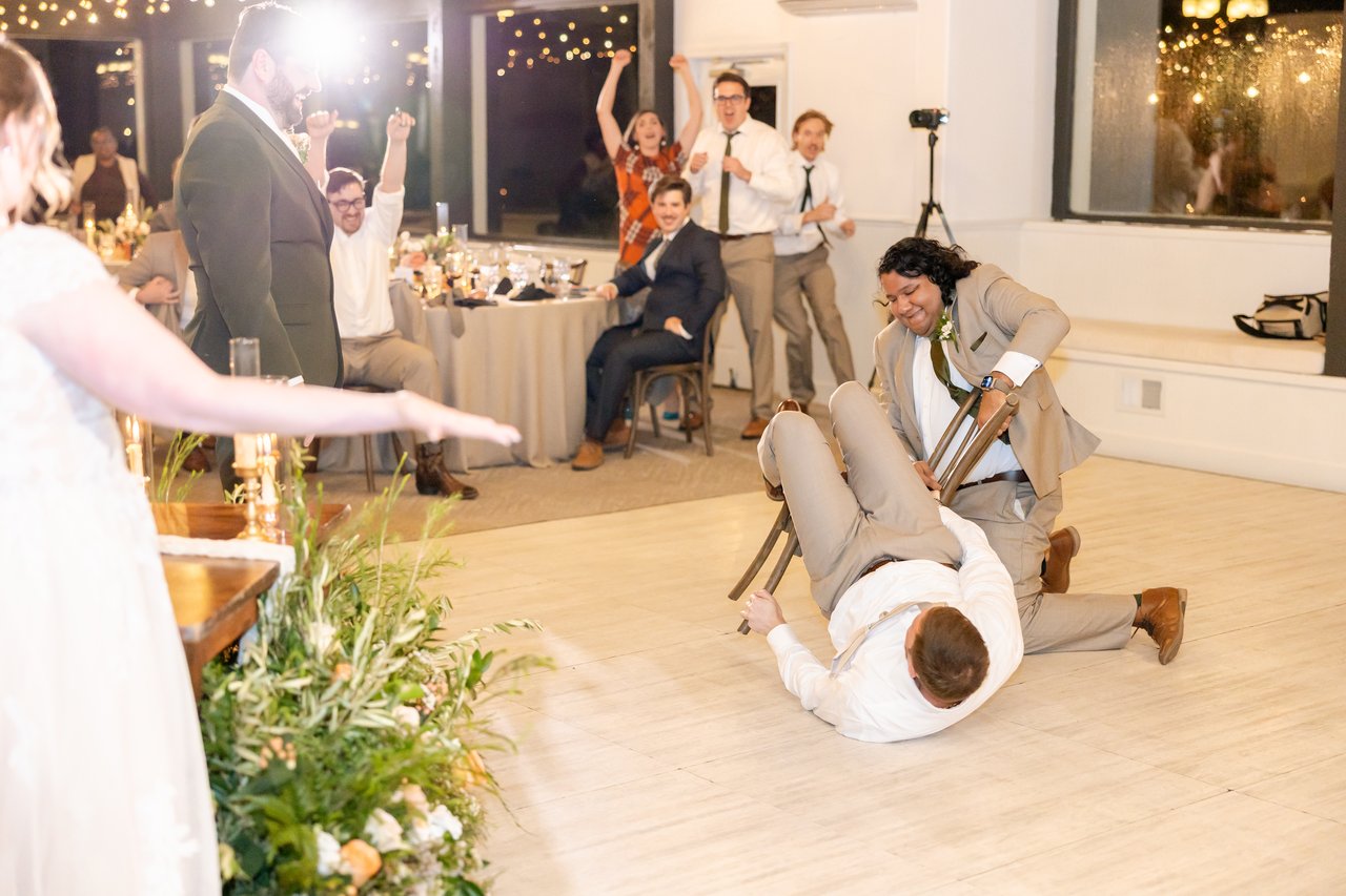 A groomsman slides across the floor with a chair during the musical chairs scavenger hunt