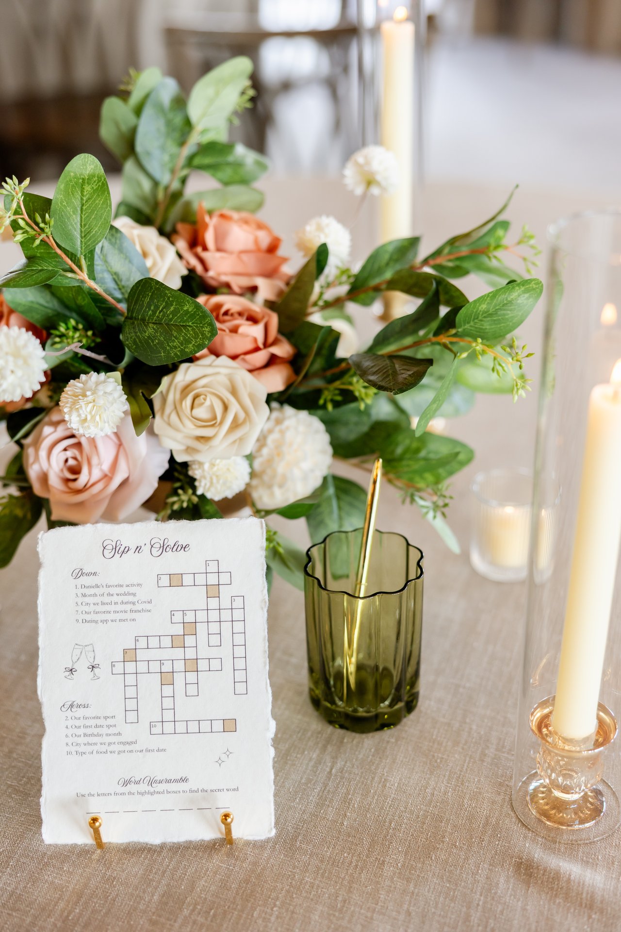 A crossword place card beside peach and ivory roses and taper candles on a guest table