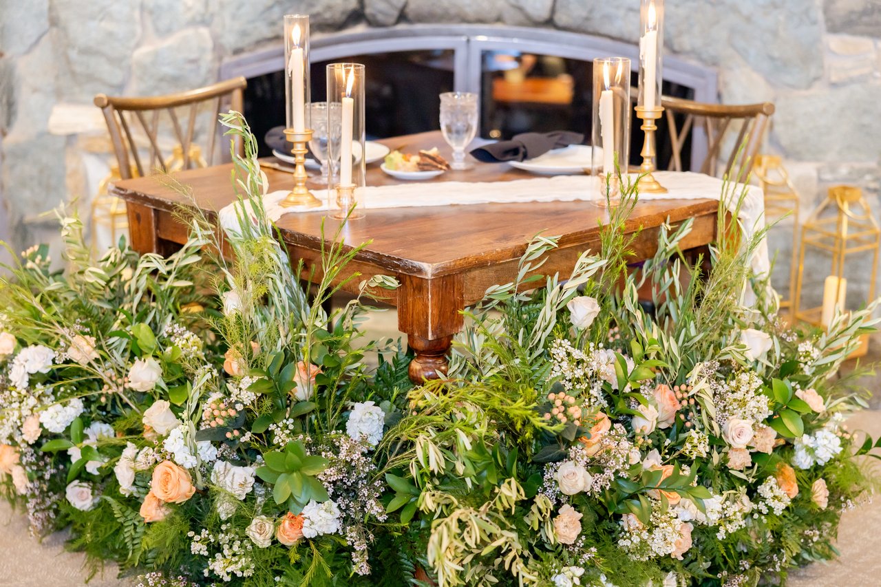 The sweetheart table in front of the stone fireplace, surrounded by wildflowers