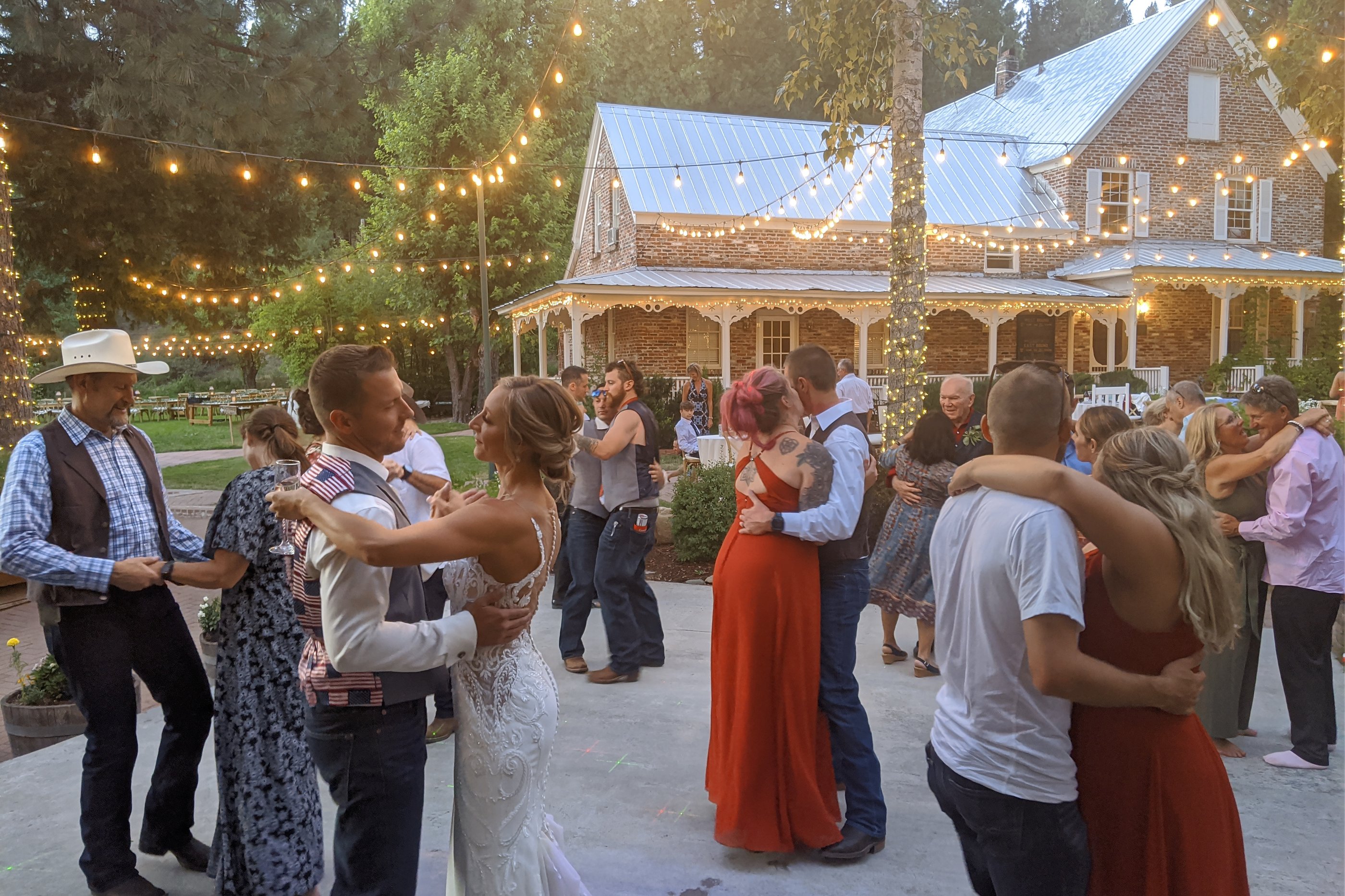 Danielle and Scott slow dance with their guests under string lights in front of the brick house at Twenty Mile House