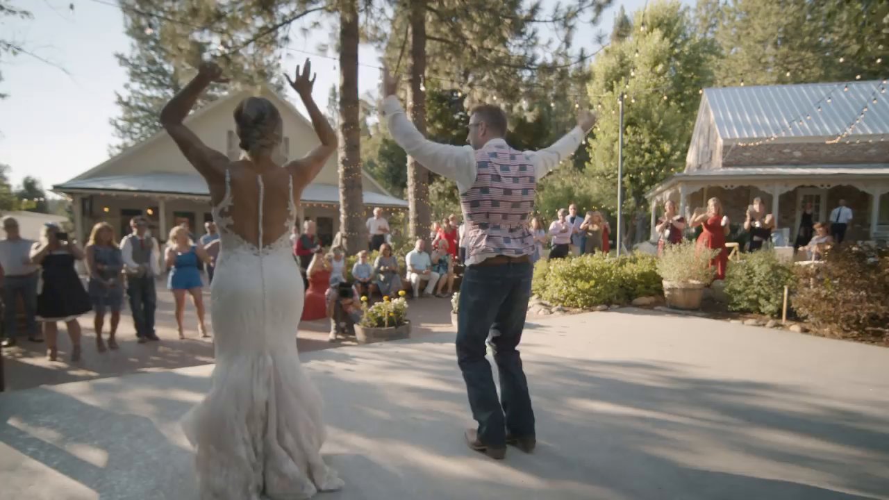 Danielle and Scott dance with their arms up on the patio as guests watch.