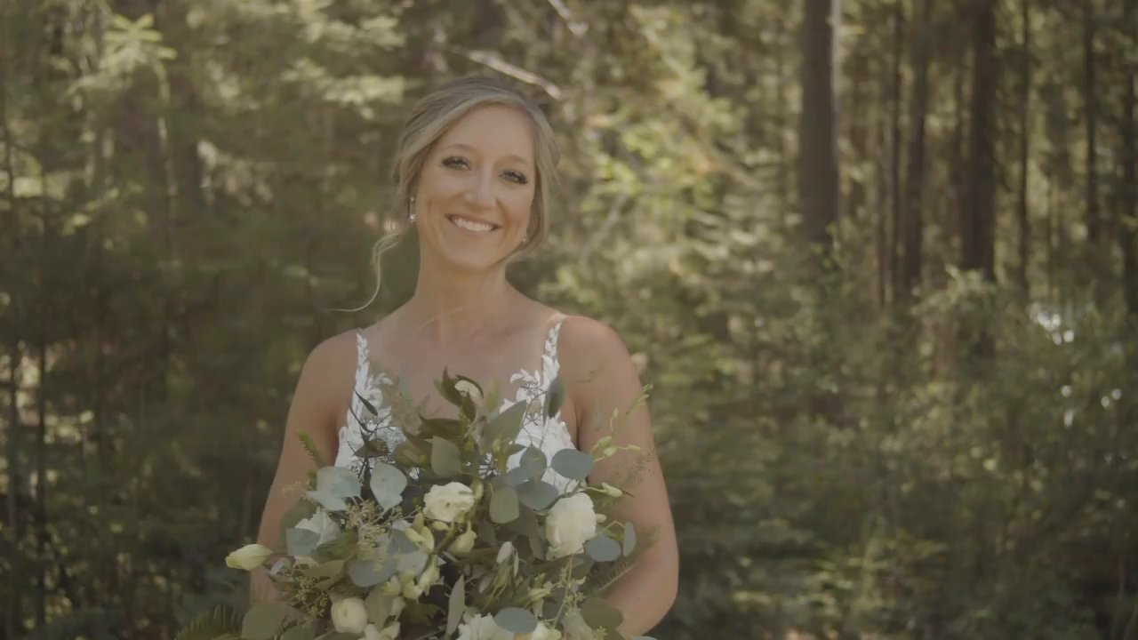 Danielle smiles in the forest holding her bouquet of white roses and eucalyptus.