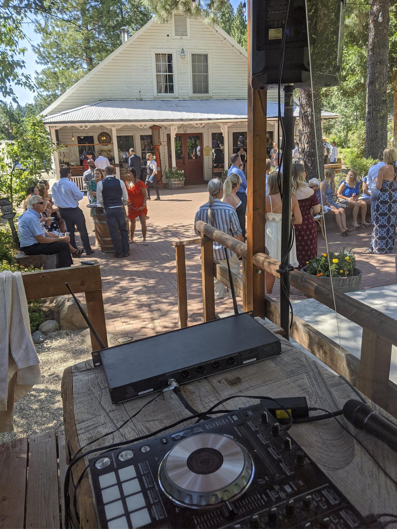 Guests mingle on the patio in front of the white house during cocktail hour, seen from behind the DJ controller