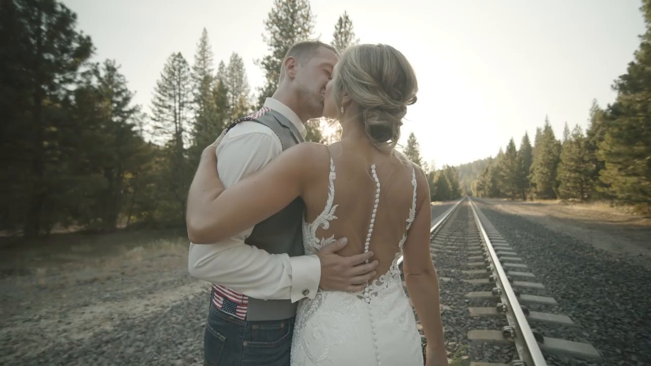 Danielle and Scott embrace beside the railroad tracks in the golden light.