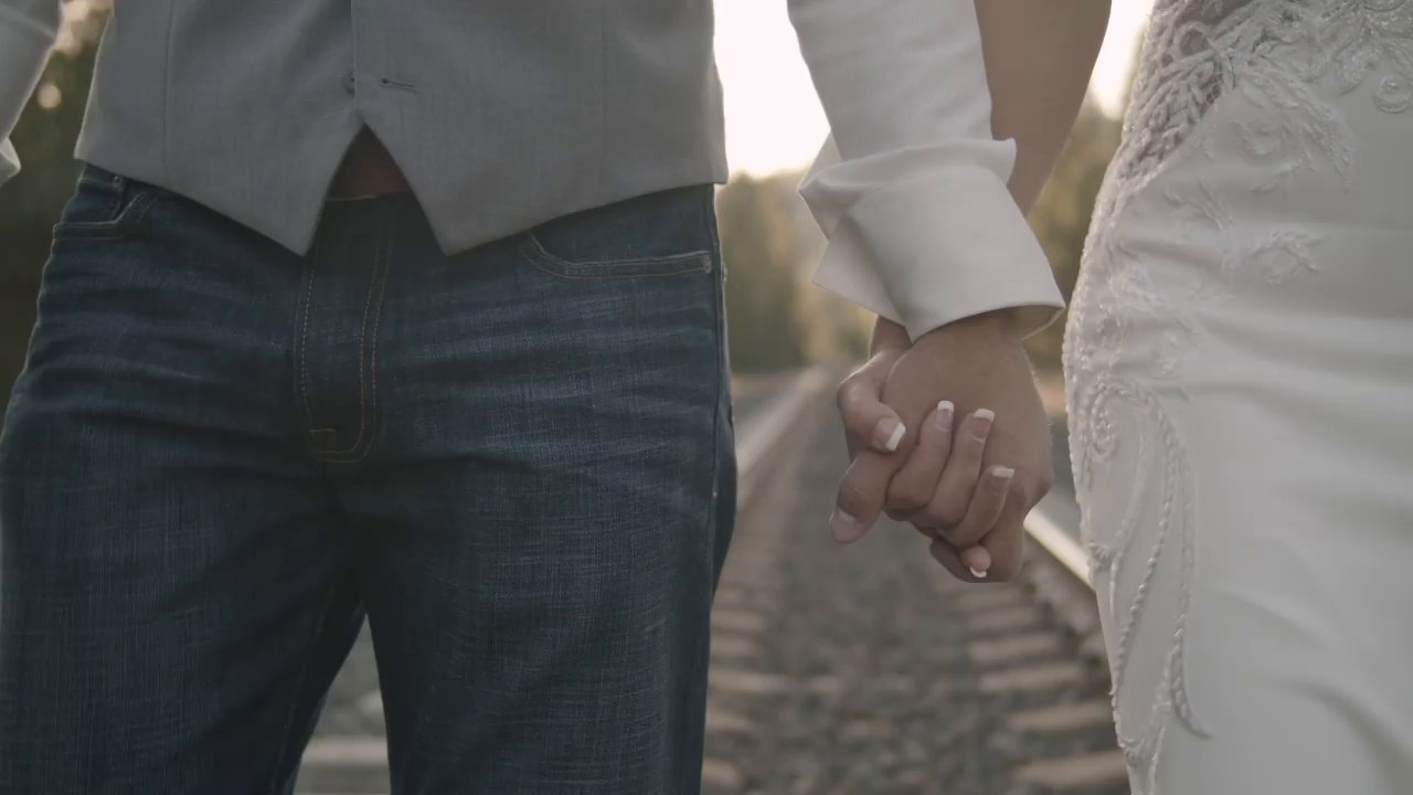 Danielle and Scott hold hands as they walk along the railroad tracks, her lace gown beside his jeans.