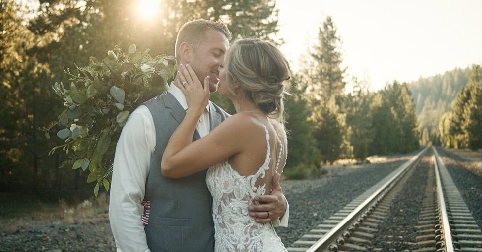 Scott holds Danielle's face as they kiss beside the railroad tracks in the golden evening light